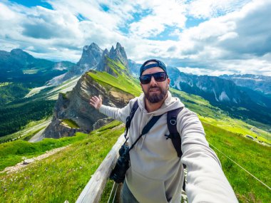 Fotoğrafçı, kollarını uzatarak selfie çekiyor. Güneşli bir yaz gününde dolomitlerin nefes kesen seceda zirvelerini ve yemyeşil vadilerini yakalıyor.