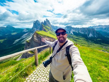 Sırt çantalı ve kameralı fotoğrafçı, İtalyan dolomitlerinin Seceda sıradağlarında uzanmış kollarıyla bir selfie portresi çekiyor.