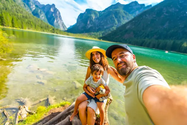 Mutlu bir aile yaz tatilinde arka planda dolomitlerle dobbiaco gölünde selfie çekiyor.