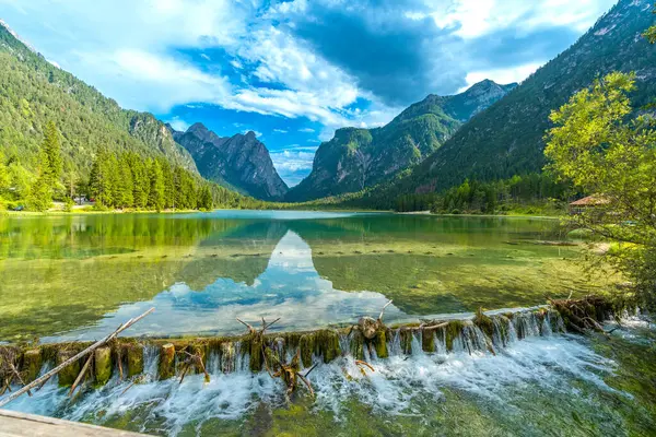 İtalya 'da güneşli bir yaz gününde görkemli dolomitlerle çevrili Dobbiaco Gölü' nden akan kristal berrak su.