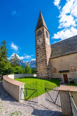 St. Magdalena Kilisesi 'ne giden açık demir kapı arka planda parlak mavi bir yaz gökyüzünün altında yükselen dağlarla birlikte.