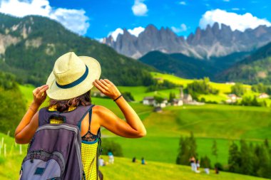 Sırt çantalı kadın turist hasır şapkasıyla dolomitlerdeki İtalyan Alplerinin nefes kesici manzarasının tadını çıkarıyor.