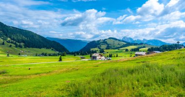 Alpe di Siusi 'de nefes kesici yaz manzarası, dolomitler, İtalya, sergilenen yemyeşil çayırlar, yuvarlanan tepeler, geleneksel evler ve canlı mavi bir gökyüzü.