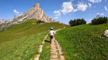 İtalyan dolomitleriyle Giau geçidinde koşan mutlu bir çocuk. Arka planda dağ zirvesi ve mavi gökyüzü var.