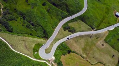 Yukardan görülen viraj yolu, İtalyan dolomitleri dağlarında yeşil bir çayırda giden arabalarla birlikte.