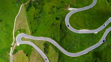Yukardan görülen viraj yolu, İtalyan dolomitleri dağlarında yeşil bir çayırda giden arabalarla birlikte.