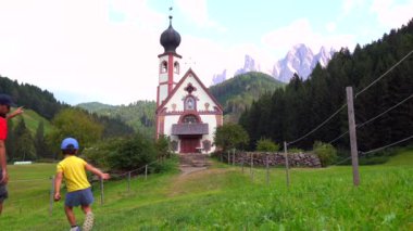 Baba ve oğul, Dolomite 'lar tarafından çerçevelenmiş fonlar içindeki görkemli St. Magdalena kilisesinin çarpıcı manzarasına hayran kalıyorlar.