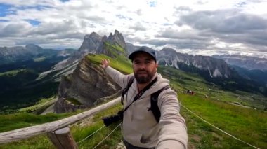 Sırt çantalı ve kameralı fotoğrafçı, İtalyan dolomitlerinin Seceda sıradağlarında uzanmış kollarıyla bir selfie portresi çekiyor.