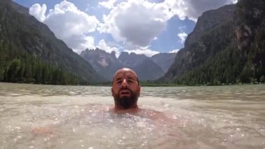 Güneşli bir yaz gününde dolomitlerin nefes kesici manzarasıyla çevrili lago di landro 'nun berrak sularında yüzen bir turist.