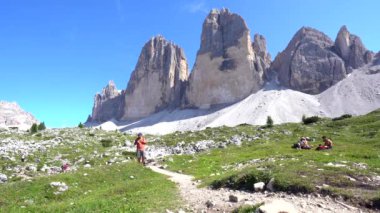 Turist, dolomitlerdeki görkemli Tre cime di lavaredo zirvelerine giden manzaralı bir yolda yaz yürüyüşünün tadını çıkarıyor.