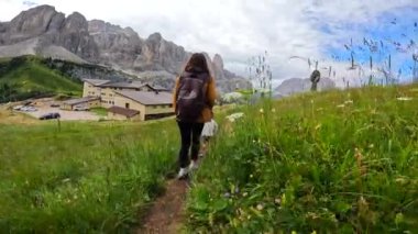 Anne ve oğul yemyeşil çimlerle çevrili bir yolda yürüyor, Dolomite dağlarının bahçedeki nefes kesen manzarasının tadını çıkarıyorlar.