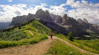 Güneşli bir yaz gününün tadını çıkaran bir kadın, gardenya geçidindeki dolomitler arasında yürürken, göz kamaştırıcı dağ manzarası ile çevrili.