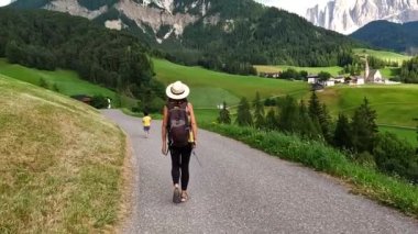 Şapkasını tutan kadın turist, Val di Funes 'daki Odin Dağları ve Santa Maddalena Kilisesi' nin çarpıcı manzarasına hayran kaldı.