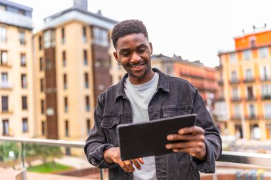 Mutlu Afrikalı adam dijital tabletin ekranına dokunuyor ve şehirde gülümsüyor.