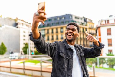 Havalı bir Afrikalı adam şehirde selfie çekerken kameraya göz kırpıyor.