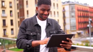 Mutlu Afrikalı adam dijital tabletin ekranına dokunuyor ve şehirde gülümsüyor.