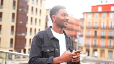 Elinde cep telefonu olan Afrikalı bir adam, arka planda şehir manzaralı bir sesli mesaj gönderiyor.