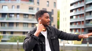 Afrikalı havalı adam kulaklıkla müzik dinliyor ve şehirde dans ediyor.