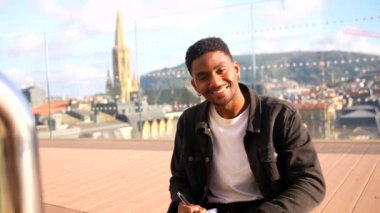 Düşünceli Afrikalı genç erkek gezgin güneşli bir günde şehrin bakış açısına notlar yazıyor.