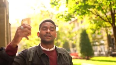 Afrikalı bir adam gün batımında şehirde cep telefonuyla fotoğraf çekiyor.