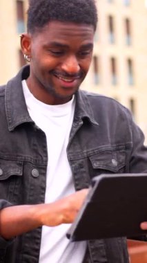 Mutlu Afrikalı adam dijital tabletin ekranına dokunuyor ve şehirde gülümsüyor.