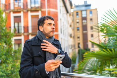 Sıcak kış giysileri içinde şehirde akıllı telefon kullanan bir iş adamı.