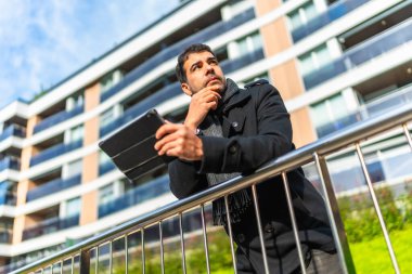 Dijital tablet kullanan, sıradan kışlık giysiler içinde, Kafkasyalı bir iş adamının düşük açılı görüntüsü.