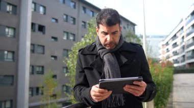 İş adamı kışlık kıyafetlerini giymiş, dijital tablet kullanıyor ve kışın şehrin dışında dikiliyor.