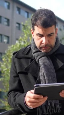 İş adamı kışlık kıyafetlerini giymiş, dijital tablet kullanıyor ve kışın şehrin dışında dikiliyor.