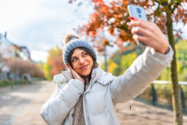 Kışın şehirde cep telefonuyla selfie çeken beyaz bir kadın.