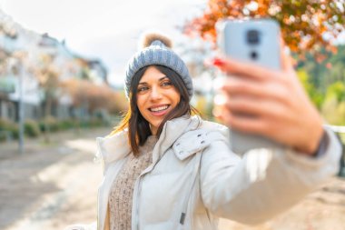 Güneşli bir kış gününde dışarıda selfie çekerken kendine güvenen bir kadın gülümsüyor.