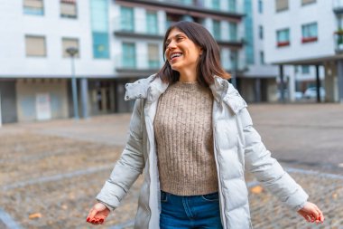 Beyaz, mutlu, kalın giysiler giyen bir kadın şehirde tek başına dans etmekten zevk alıyor.