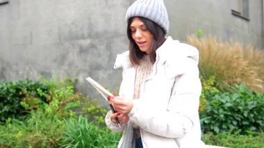 Genç bir kadın şehirde bir bankta oturmuş deftere yazı yazıyor.