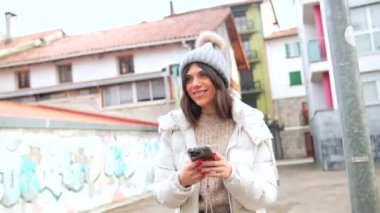 Şehirde kışın telefon kullanan, kalın elbiseli, mutlu, beyaz bir kadın.