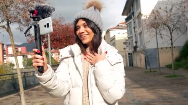 Güneşli bir sonbahar gününde şehirde cep telefonu kullanarak çevrimiçi yayınlanan sevimli beyaz kadın vlogger.