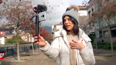 Beyaz tenli kadın video blogcusu şehirdeki izleyicilere çevrimiçi video kaydediyor.