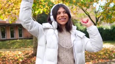 Güneşli bir sonbahar gününde parkta telefon kullanan ve müzik dinleyen beyaz bir kadın.