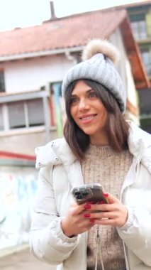 Şehirde kışın telefon kullanan, kalın elbiseli, mutlu, beyaz bir kadın.