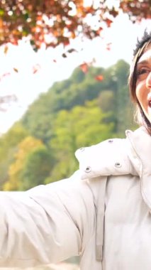 Beyaz tenli, genç ve güzel bir kadın vlogger. Sıcak kışlık giysiler giyip şehir parkında video kaydediyor.