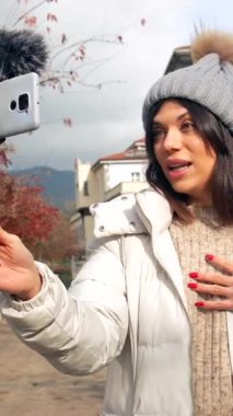 Beyaz tenli kadın video blogcusu şehirdeki izleyicilere çevrimiçi video kaydediyor.