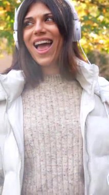 Parkta müzik dinleyip dans eden güzel beyaz bir kadının sonbaharın tadını çıkarırken ön görüntüsü.