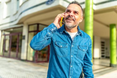 Kot elbiseli, gülümseyen ve caddedeki cep telefonuyla konuşan mutlu olgun bir adam.