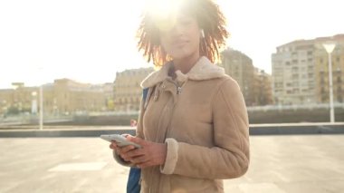 Mutlu genç latin telefon kullanarak ve müzik dinleyerek gün batımında şehirde durarak