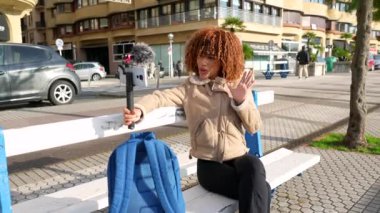Şehirde şehir merdivenlerinde otururken, Latin bir kadın vlogger izleyicilerle çevrimiçi konuşuyor.