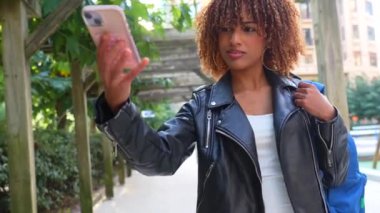 Latin güzeli genç kadın şehirde yürürken selfie çekiyor.