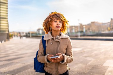 Güzel genç Latin kadın şehirde bir yön bulmak için cep telefonu kullanıyor.