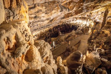Turistler, Slovenia 'daki ünlü post-jna mağarasını gezerek sarkıtlar ve dikitler arasında yürüyüş yapıyorlar.