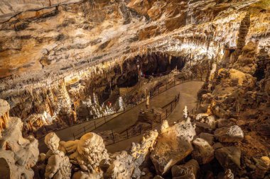 Turistler, post-jna mağarasının içinde aydınlık patikada yürüyorlar. Postojna, Slovana yakınlarındaki bir karst mağara sistemi.