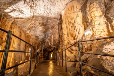 Aydınlatılmış yolda yürüyen turistler posta mağarasının içindeki sarkıt ve dikitlere hayranlık duyuyorlar. Bu, Slovenistan 'ın ünlü doğal cazibesidir.