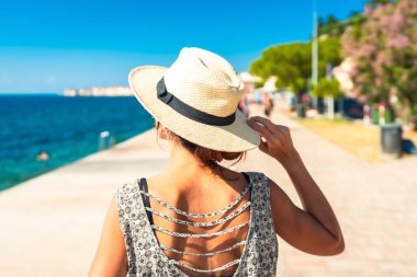 Hasır şapkalı genç bir kadın Piran, Slovenia 'nın güvertesinde yürüyor, Adriyatik sahillerinde yaz tatilinin tadını çıkarıyor.